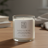 Candle labeled '1889 Nocturne' on a wooden surface with a blurred background