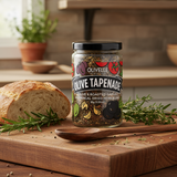 Jar of Olivelle Olive Tapenade on a wooden cutting board with bread and herbs.