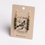 A pair of dangling earrings with green faceted beads and gold hooks, displayed on a kraft paper card printed with the brand name Lady Bird.