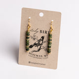 A pair of dangling earrings with green faceted beads and gold hooks, displayed on a kraft paper card printed with the brand name Lady Bird.