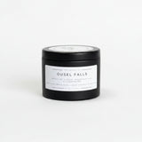 A black cylindrical candle tin with a white label reading 'OUSEL FALLS' sits on a white background