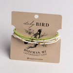 Three beaded bracelets in light green, white, and gold tones displayed on a brown kraft card labeled Lady Bird, photographed against a light neutral background.