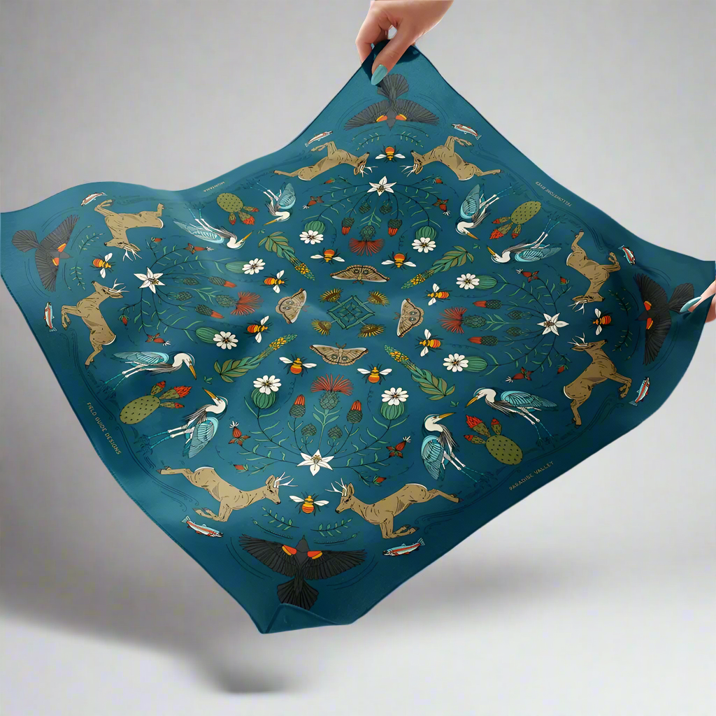 Decorative scarf with animal and nature pattern held by a hand against a white background