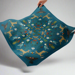 Decorative scarf with animal and nature pattern held by a hand against a white background