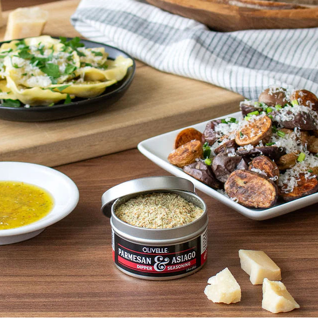 Table setting with plates of food, a container of Parmesan & Asiago seasoning, and bread.