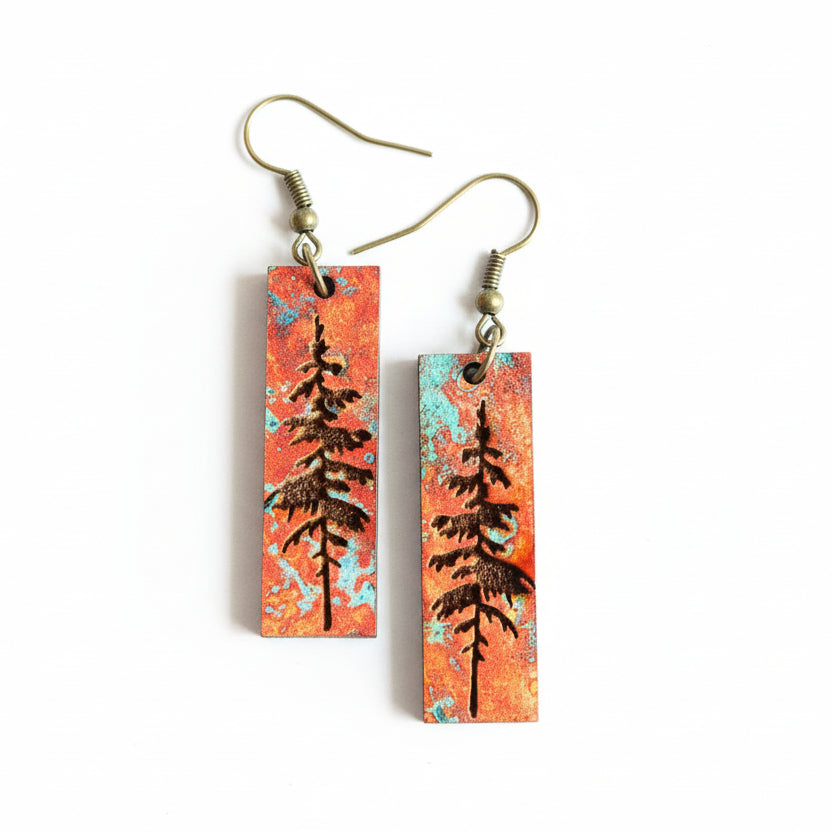 Pair of earrings with tree design on a white surface with flowers