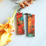 Colorful marbled earrings on a white surface with yellow flowers.