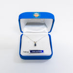 A silver necklace with a small blue sapphire pendant is displayed inside an open blue jewelry box with a white satin lining. The box has a 'YOGO JEWELRY USA' logo on the inside lid and a '14KW YOGQ SAPPHIRE' label on the front.