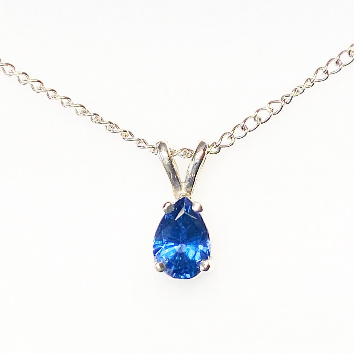 A silver chain necklace with a pear-cut blue gemstone pendant in a silver setting, shown against a plain white background.