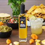 Olivelle Pineapple Habanero hot sauce bottle with a cocktail, guacamole, and chips on a wooden table.