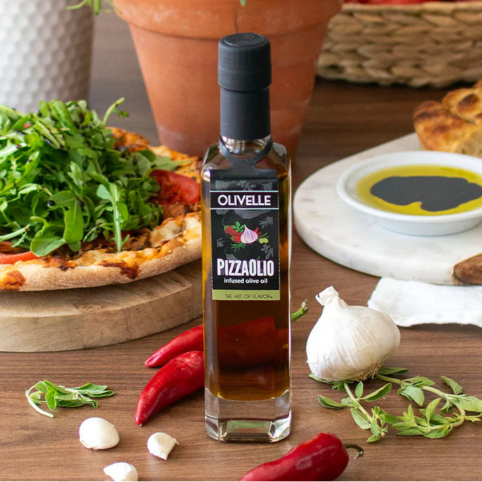 Olive oil bottle labeled 'Pizzaiolo' on a table with pizza, bread, and vegetables.