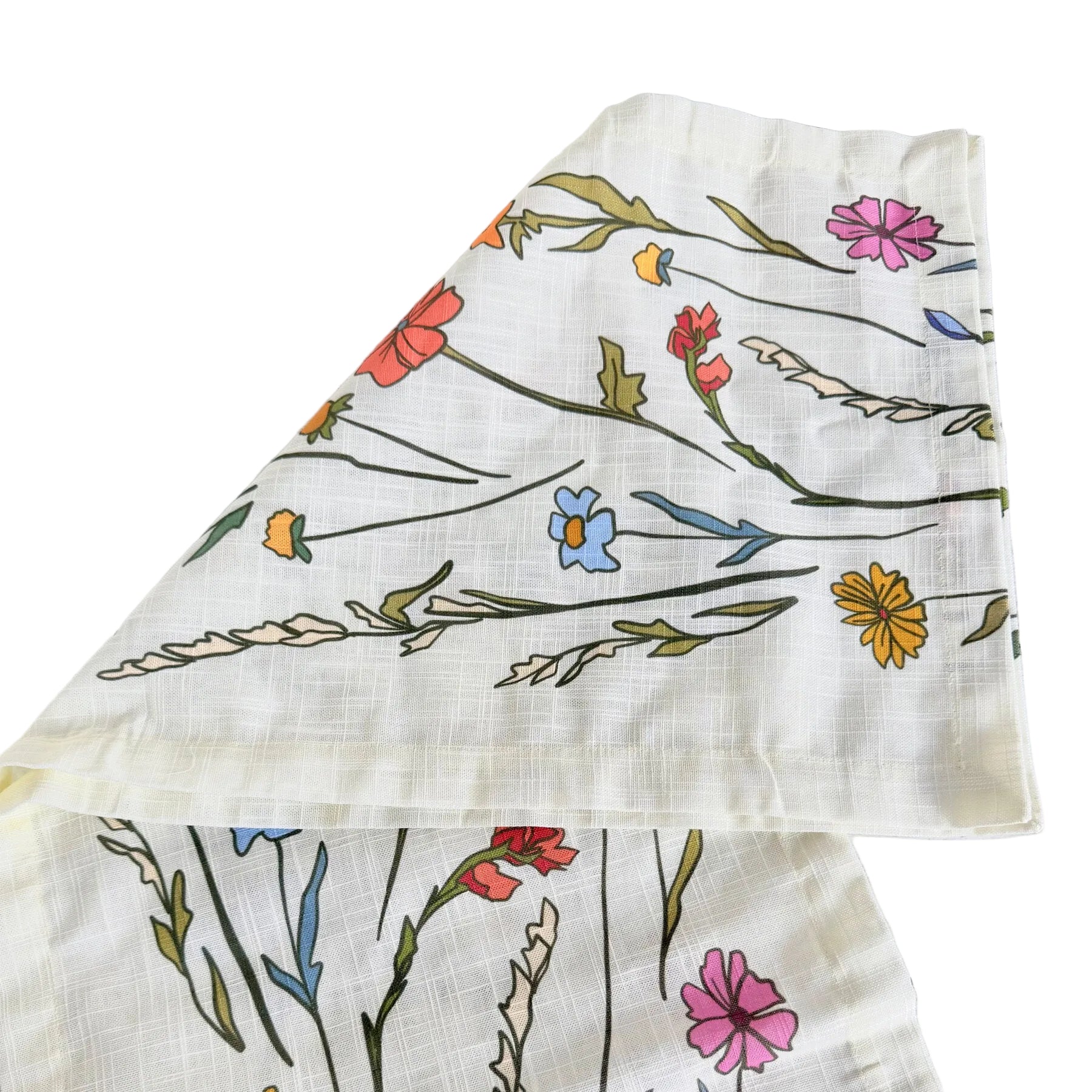 A folded cream-colored cotton muslin cloth with a colorful wildflower print, displayed on a white-washed wooden background.