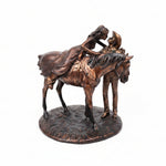 A dark bronze sculpture of a cowboy riding a bucking horse, mounted on a round textured base, photographed on a brown cutting mat.