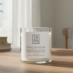 Candle labeled '1889 Preacher' on a wooden surface with a blurred background
