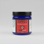 A jar of Natural Encouragement 'Ripped' sore muscles and joints cream, featuring a dark blue jar, black lid, and red label, set on a rustic wooden surface.