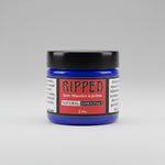 A small jar of Ripped Sores, Muscles & Joints Natural Essentials cream sits on a rustic, weathered wooden surface.