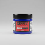 A small jar of Ripped Sores, Muscles & Joints Natural Essentials cream sits on a rustic, weathered wooden surface.