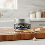 Jar of roasted garlic infused sea salt on a wooden cutting board with garlic cloves in a kitchen setting.