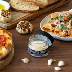 Roasted garlic spread jar with bread, pizza, and pasta on a wooden table