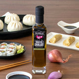 Olivelle Roasted Shallot olive oil bottle on a wooden table with sushi, dumplings, and shallots.