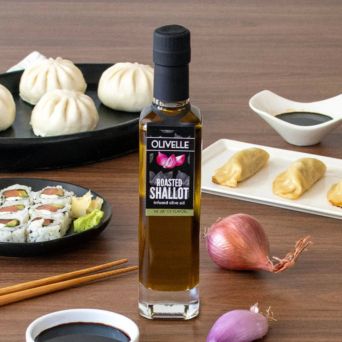 Olivelle Roasted Shallot olive oil bottle on a wooden table with sushi, dumplings, and shallots.