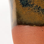 handcrafted mug with a blue and tan glaze that colors half of the piece. the bottom is uncovered. on a white background