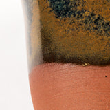 handcrafted mug with a blue and tan glaze that colors half of the piece. the bottom is uncovered. on a white background