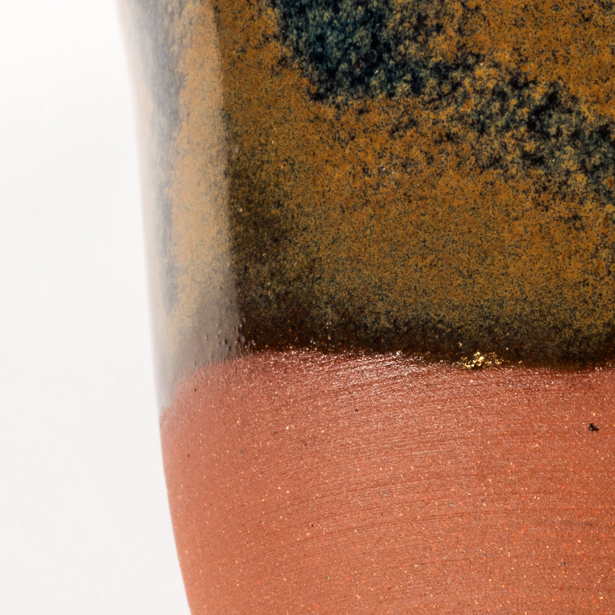 handcrafted mug with a blue and tan glaze that colors half of the piece. the bottom is uncovered. on a white background