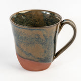 handcrafted mug with a blue and tan glaze that colors half of the piece. the bottom is uncovered. on a white background