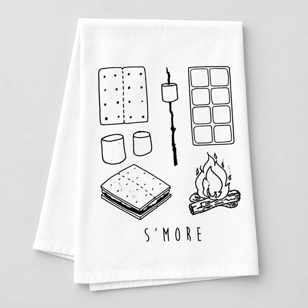 A white kitchen towel with black line art illustrations of s'mores (graham crackers, marshmallows, ice cream, s'more stack, campfire) and the text 'S'MORE' at the bottom, laid flat on a wooden surface.