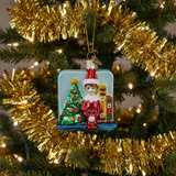 Christmas ornament of an elf by a decorated tree with gold tinsel