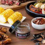 Table with smoked bacon seasoning, corn on the cob, grilled chicken, and various meats and vegetables.