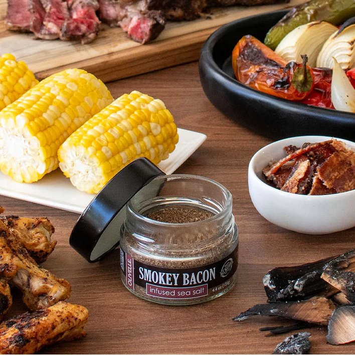 Table with smoked bacon seasoning, corn on the cob, grilled chicken, and various meats and vegetables.