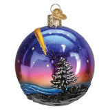 Glass ornament with a winter scene including a tree, sunset, and rainbow, on a white background.