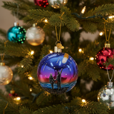 Decorative Christmas ornament with a couple watching the sunset on a mountain, hanging on a tree.