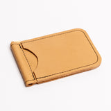A minimalist tan leather money clip wallet with black contrast stitching, shown on a clean white background.