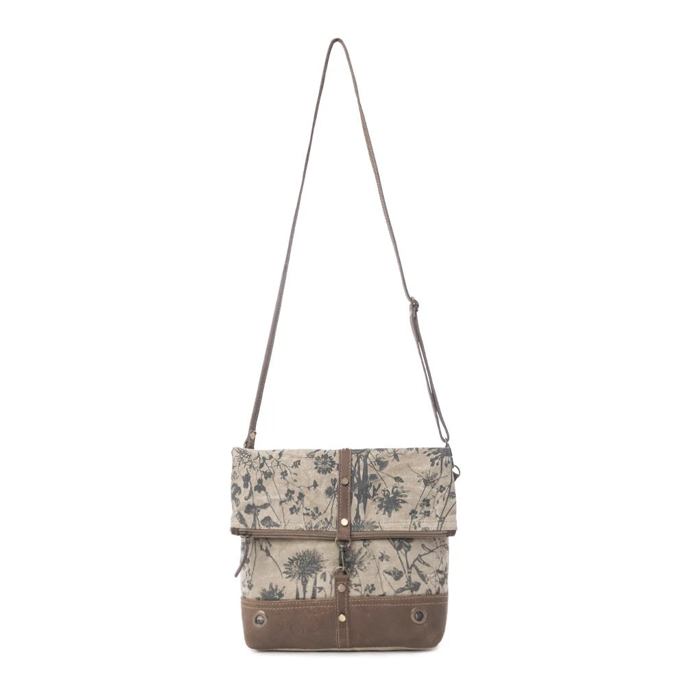 A canvas shoulder bag with a brown floral print and brown leather trim, featuring a long adjustable shoulder strap and a front flap closure with metal snap details, shown against a plain white background.