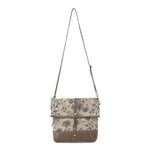 A canvas shoulder bag with a brown floral print and brown leather trim, featuring a long adjustable shoulder strap and a front flap closure with metal snap details, shown against a plain white background.