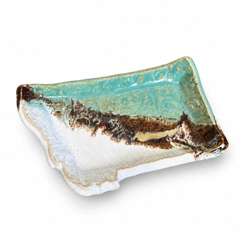 A rectangular ceramic tray with a rustic, hand-painted finish, featuring a turquoise glaze on the top half, a white textured glaze on the bottom half, and a dark brown crackled border. The tray is displayed on a dark wood tabletop.