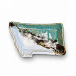 A rectangular ceramic tray with a rustic, irregular edge, featuring a glossy turquoise and white glaze with a dark brown metallic-looking crackled pattern. The tray is displayed on a dark brown wooden table against a light beige wall.