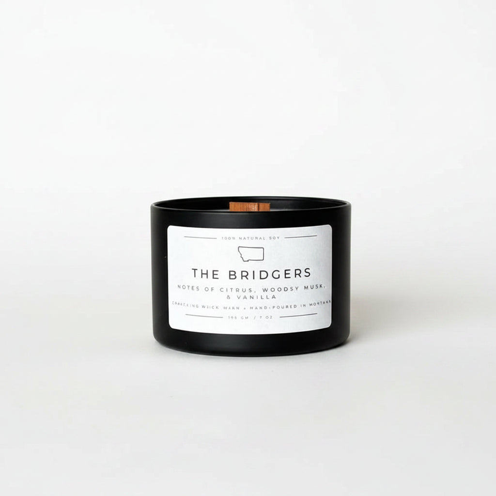 A black glass jar candle with a white label reading 'THE BRIDGERS' and a small copper-colored wick, set on a white background.