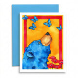 A square art print or greeting card featuring a watercolor-style blue bear looking upward, with blue butterflies, a red border, and red flowers on a yellow background. A blue envelope is placed behind the card on a white studio background.
