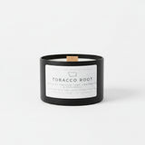 A black candle jar labeled Tobacco Root by 1841 Natural Co., with a small wood wick and a white front label, sitting on white studio background