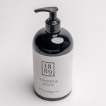 A 1889 brand Trapper hand cream bottle with a glossy black body and pump dispenser, featuring a white label with black text, set against a clean white background.