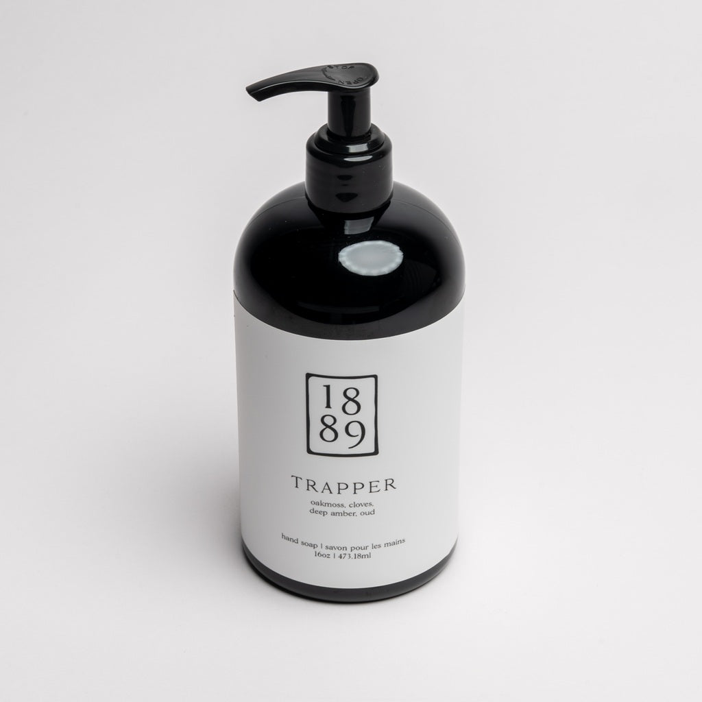 A black pump bottle with a white label for 1889 Trapper Hand & Body Wash, photographed on a clean white background.