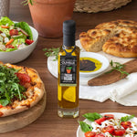 Olivelle Tuscan Herb olive oil bottle on a wooden table with pizza, salad, and bread.