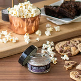 Vanilla bean infused sea salt jar with popcorn, cookies, and brownies on a wooden surface