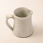 Speckled ceramic pitcher on a beige background