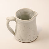 Speckled ceramic pitcher on a beige background