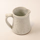 Speckled ceramic pitcher on a beige background